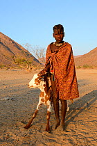 Himba girl with traditional double plait hairstyle with goat. Marienfluss Valley, Kaokoland Desert, Namibia. October 2015