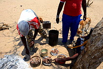 Himba men distributing freshly cooked meat, Marienfluss Valley, Kaokoland Desert, Namibia. October 2015