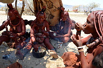 Himba women eating meal of goat meat together, Marienfluss Valley, Kaokoland Desert, Namibia. October 2015