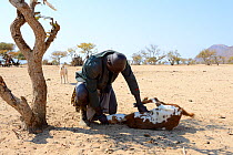 Himba man killing a goat by suffocating it, Marienfluss Valley, Kaokoland Desert, Namibia. October 2015