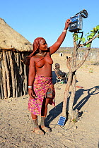 Himba woman turning on her solar powered radio, Etanga, Kaokoland, Namibia. October 2015