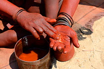 Himba woman mixing ochre with butter to make Otjize, Marienfluss Valley. Kaokoland, Namibia. October 2015