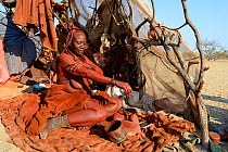 Himba woman in her temporary hut applying Otjize (a mixture of butter, ochre and ash) to her skin. Marienf luss valley. Kaokoland, Namibia October 2015