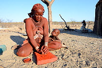 Himba woman crushing ochre into powder, Marienfluss Valley. Kaokoland, Namibia October 2015