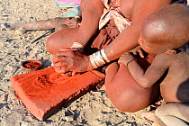 Himba woman crushing ochre into powder, Marienfluss Valley. Kaokoland, Namibia October 2015