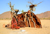 Himba woman sitting beside temporary hut with fire in front, Marienfluss Valley. Kaokoland, Namibia. October 2015