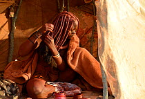Himba woman applying Otjize (a mixture of butter, ochre and ash) to her hair. Marienfluss Valley. Kaokoland, Namibia October 2015