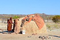 Himba woman beside traditional mud hut. Kaokoland, Namibia. October 2015