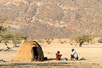 Himba family beside traditional mud hut, Marienfluss Valley during the dry season. Kaokoland, Namibia. October 2015