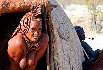 Portrait of Himba woman emerging from her hut, Kaokoland, Namibia October 2015