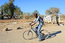 Himba teenage boy living, in a modern western clothing on bicycle, Opuwo, Kaokoland, Namibia. October 2015
