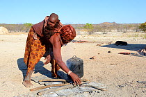 Himba woman with baby preparing the fireplace, Etanga, Kaokoland Desert, Namibia. October 2015