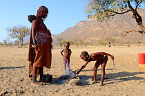 Himba girl starting fire with her mother for the cooking, Marienfluss Valley, Kaokoland Desert, Namibia. October 2015