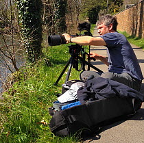 Portrait of wildlife photographer and filmmaker Nick Upton taking photos on riverbank.