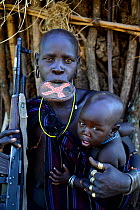 Mursi woman with clay lip plate, holding rifle and son. Mago National Park. Omo Valley, Ethiopia.
