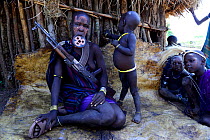 Mursi woman with clay lip plate  and children, armed with rifle. Mago National Park. Omo Valley, Ethiopia.