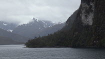 Tracking shot of a fjord landscape seen from a boat, with snow covered mountains in the background, Patagonia, Chile.