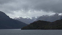 Tracking shot of a fjord landscape seen from a boat, with snow covered mountains in the background, Patagonia, Chile.