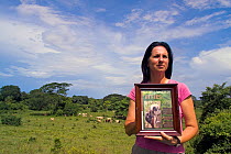Anne Savage, director of Project / Proyecto Titi holding up picture of  Cotton top tamarin (Saguinus oedipus) in pasture which was once prime tropical dry forest habitat for the monkeys, Colombia. Jul...