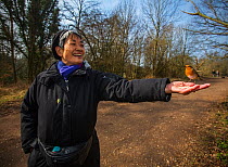 Heath walker with European robin (Erithacus rubecula) feeding directly from hand, Hampstead Heath, London, England, UK. March 2015.