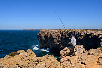 Fisherman angling in the Atlantic sea from high cliffs at Ponta de Sagres, Algarve, Portugal, July 2013.