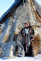 Carolina Serotetto, Nenet teenager at entrance of reindeer fur covered tent, warmly dressed in traditional coat. Yar-Sale district. Yamal, Northwest Siberia, Russia. April 2016.