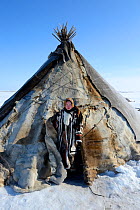 Carolina Serotetto, Nenet teenager at entrance of reindeer fur covered tent, warmly dressed in traditional coat. Yar-Sale district. Yamal, Northwest Siberia, Russia.  April 2016.