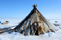 Carolina Serotetto, Nenet teenager standing at entrance of her reindeer fur covered tent, warmly dressed in traditional coat. Yar-Sale district. Yamal, Northwest Siberia, Russia. April 2016.