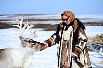Carolina Serotetto, Nenet teenager dressed in traditional winter coat made of reindeer skin with  pet ""akva"" Reindeer (Rangifer tarandus). Yar-Sale district, Yamal, Northwest Siberia, Russia. April...