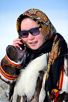 Carolina Serotetto, Nenet teenager wearing sunglasses and  traditional winter coat of reindeer fur holding smartphone. Yar-Sale district, Yamal, Northwest Siberia, Russia. April 2016.