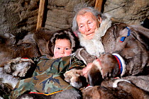 Nenet elder with grandson dressed in winter coats, made from reindeer skin in tent. Yar-Sale district, Yamal, Northwest Siberia, Russia. April 2016.