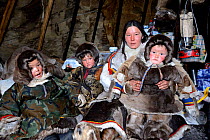 Nenet herder inside tent with daughter and sons, wearing coats made with reindeer skin and fur. Yar-Sale district. Yamal, Northwest Siberia, Russia. April  2016.