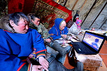 Nenet herders watching laptop inside tent. Yar-Sale district, Yamal, Northwest Siberia, Russia. April 2016.
