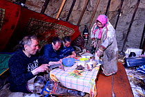 Nenet reindeer herders, eating bread, raw reindeer meat and tea inside reindeer skin tent. Yar-Sale district, Yamal, Northwest Siberia, Russia. April 2016.