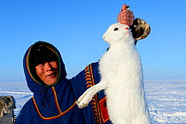 Nenet herder holding arctic hare (Lepus timidus) caught in the tundra. Yar-Sale district. Yamal, Northwest Siberia, Russia. April  2016.