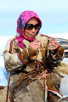 Nenet woman spinning reindeer sinew to sew reindeer skin. Yar-Sale district. Yamal, Northwest Siberia, Russia. April 2016.