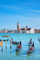 Gondolas and passengers apporac the Riva Degli Schiavoni with the Isle of San Giorgio Maggiore in distance, Venice, Italy.