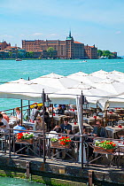 Diners on floating pontoon restaurant with Hilton Molino Stucky Venice on Giudecca Island in distance, Italy, April.