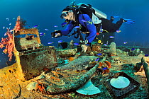 A diver on the wreck of the Shinkoku Maru, a tanker colonized by corals, sponges and other invertebrates, with various remains on the foreground such as bottles, pots and lighting a medical first aid...