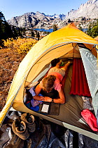 Woman Camper reading in tent above Island Lake, Wind River Range, Bridger Wilderness, Bridger National Forest, Wyoming, USA. September 2015. Model released.