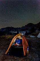 Camper reading inside tent above Island Lake, Wind River Range, Bridger Wilderness, Bridger National Forest, Wyoming, USA. September 2015. Model released.