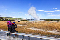 Tourists watching Old Faithful Geyser in Upper Geyser Basin, Yellowstone National Park, Wyoming, USA. September 2015.