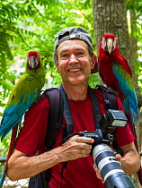 German wildlife photographer Konrad Wothe with Military macaw (Ara militaris) and Red and green macaw (Ara chloroptera) and his camera, Trinidad