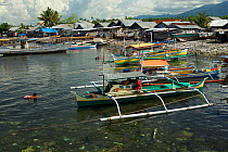 Litter strewn beach with houses and outrigger boats at Tobelo Town, Halmahera, Indonesia. July 2008.