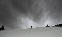 Skier on slopes with dark skies above, Jura, Switerland, March.