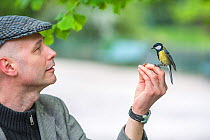 Man with Great tit (Parus major) perched on hand, in urban park, Grenoble, France. Model released