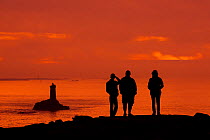 Tourists watching the lighthouse La Vieille in the strait Raz de Sein silhouetted against sunset at the Pointe du Raz, Plogoff, Finistere, Brittany, France, September.