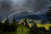 Photographer taking picture of rainbow and stormy sky over an Alpine meadow. Fiss Valley. Nordtirol, Tirol, Austrian Alps, Austria,  July 2015.