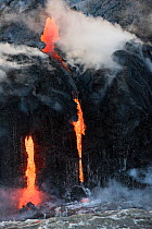 Hot lava from the 61G flow, emanating from Pu'u O'o on Kilauea Volcano, flows over sea cliffs and into the ocean through lava tubes at the Kamokuna ocean entry in Hawaii Volcanoes National Park, Kalap...