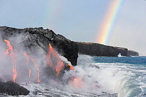 Hot lava from the 61G flow, emanating from Pu'u O'o on Kilauea Volcano, flows through lava tubes into the ocean in front of a double rainbow at the Kamokuna ocean entry in Hawaii Volcanoes National Pa...
